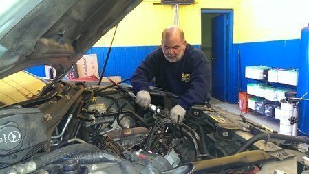 Mechanic working on a car engine in a garage. He is wearing gloves. Yellow and blue walls.