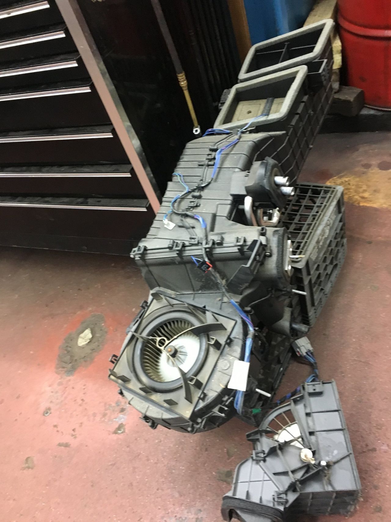 Car's air conditioning system disassembled on a shop floor, showing ducts, fan, and other components.