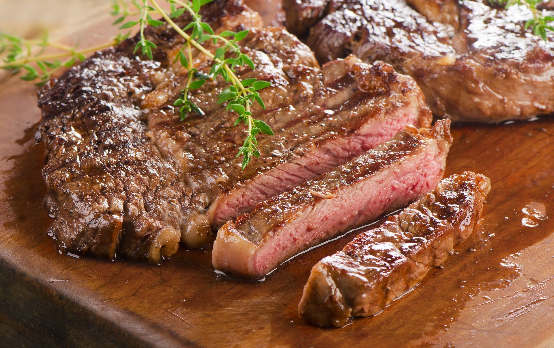 Grilled steak, sliced to show pink interior, garnished with thyme on a wooden board.