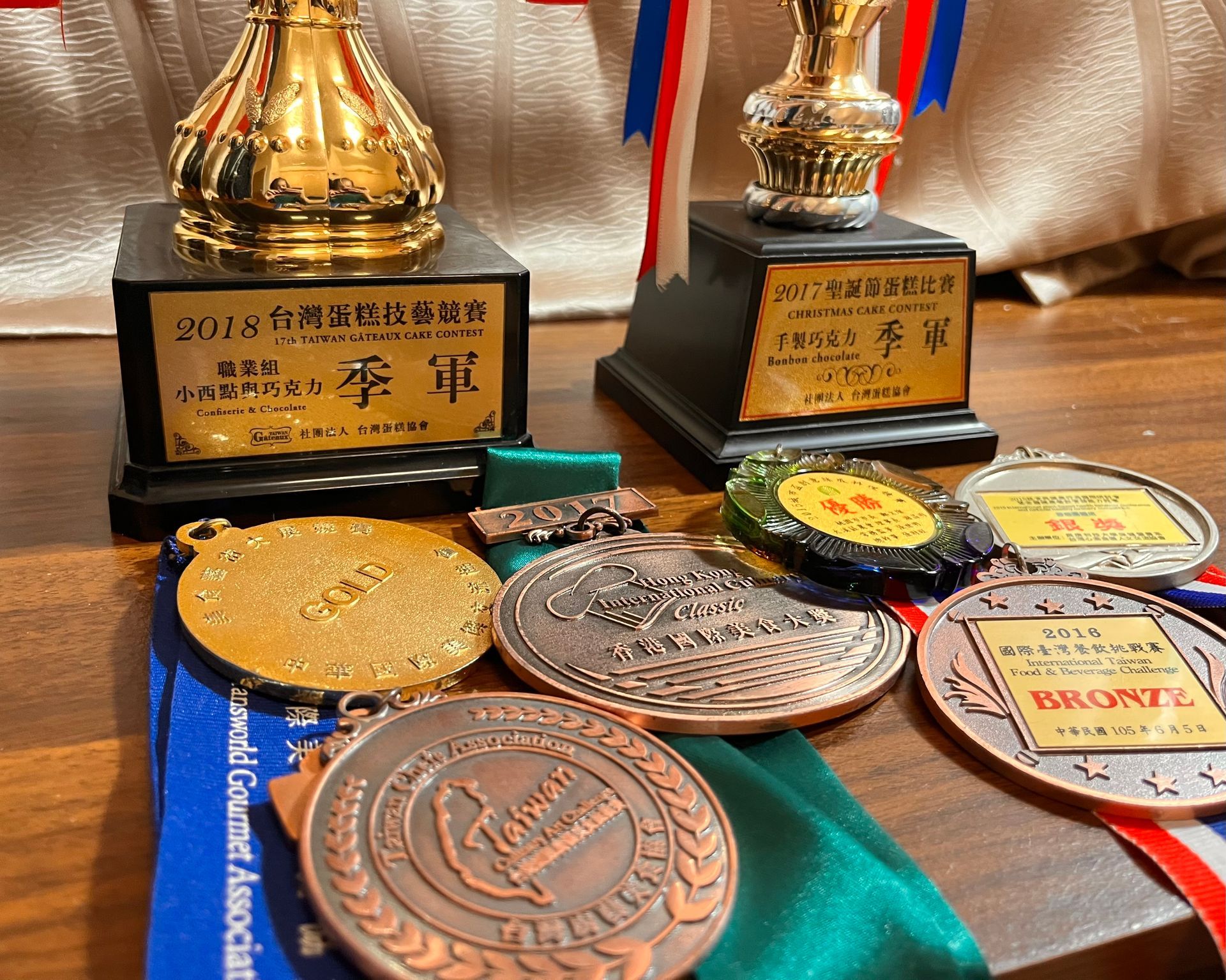 獎盃和獎牌擺放在桌面上。兩座金色獎盃放在黑色底座上，還有幾面繫著彩色瑤帶的獎牌。