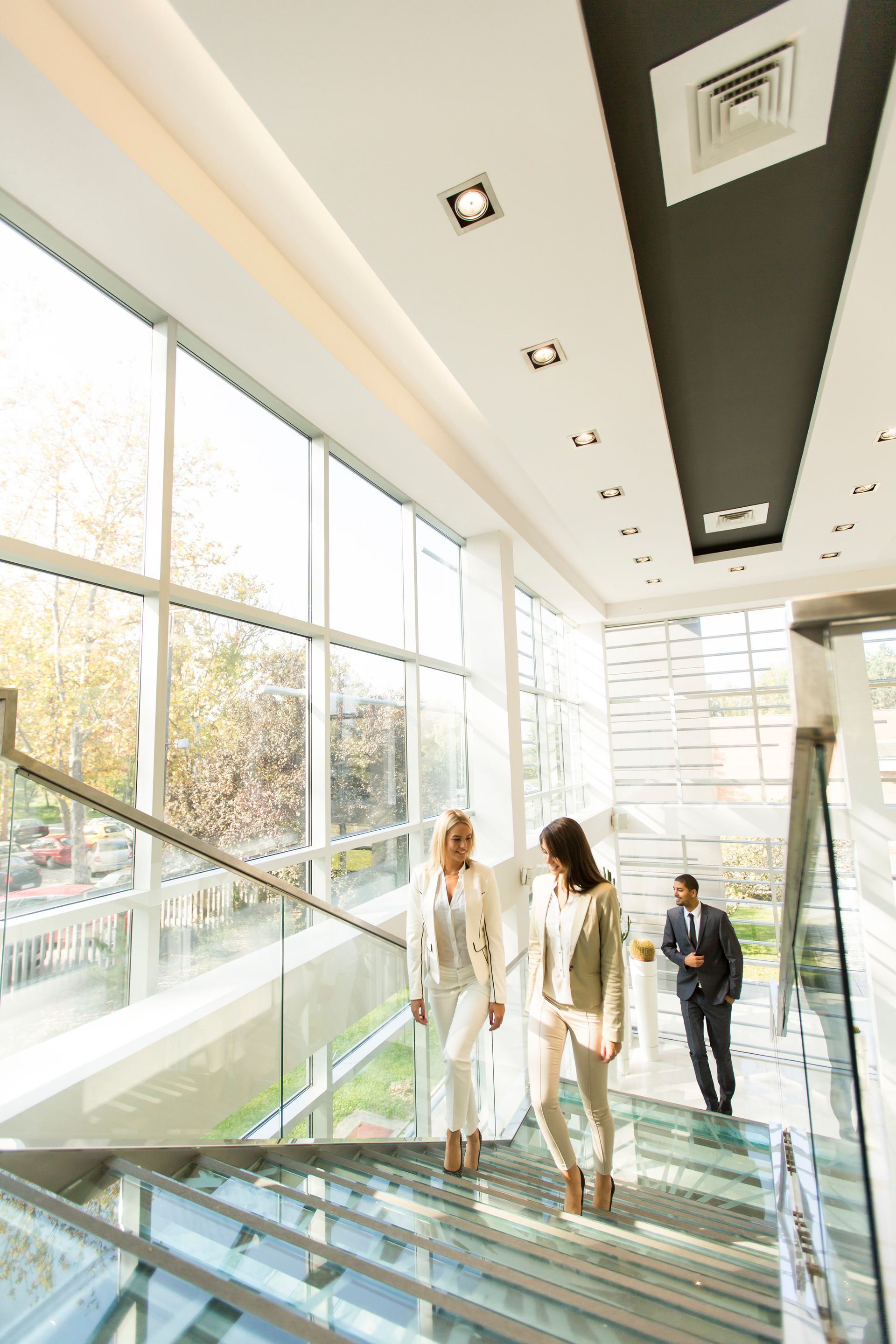 People walking up glass stairs in a bright modern atrium with large windows.