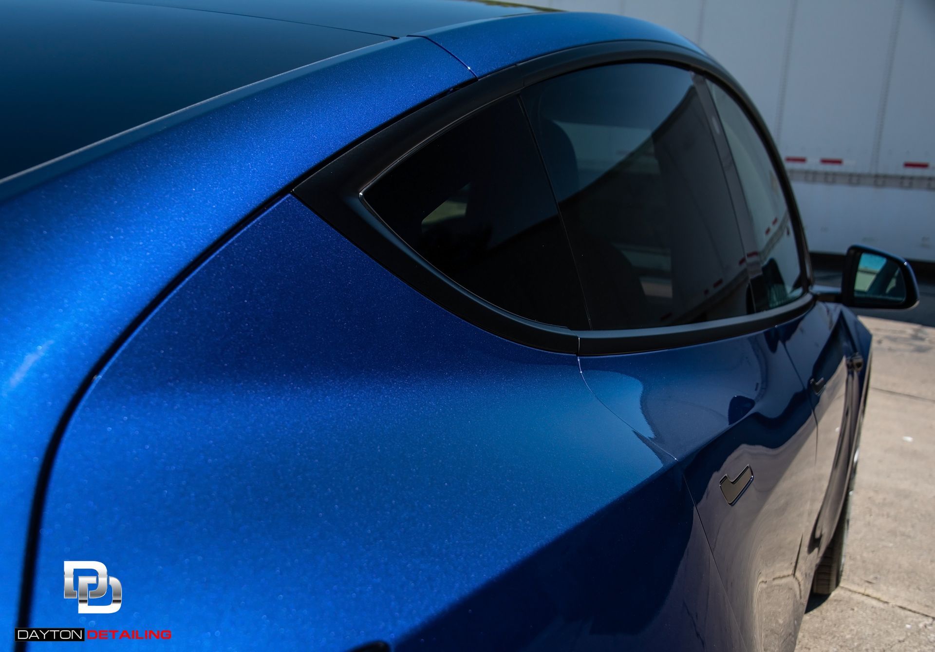 Blue electric car's side, showcasing a glossy paint job reflecting light, with tinted windows and a black trim.