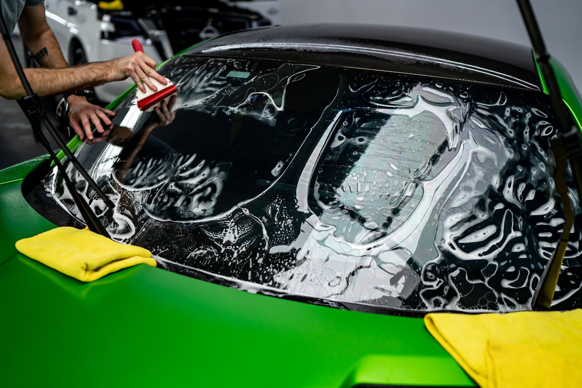 Car windshield being washed with soap and water on a bright green sports car