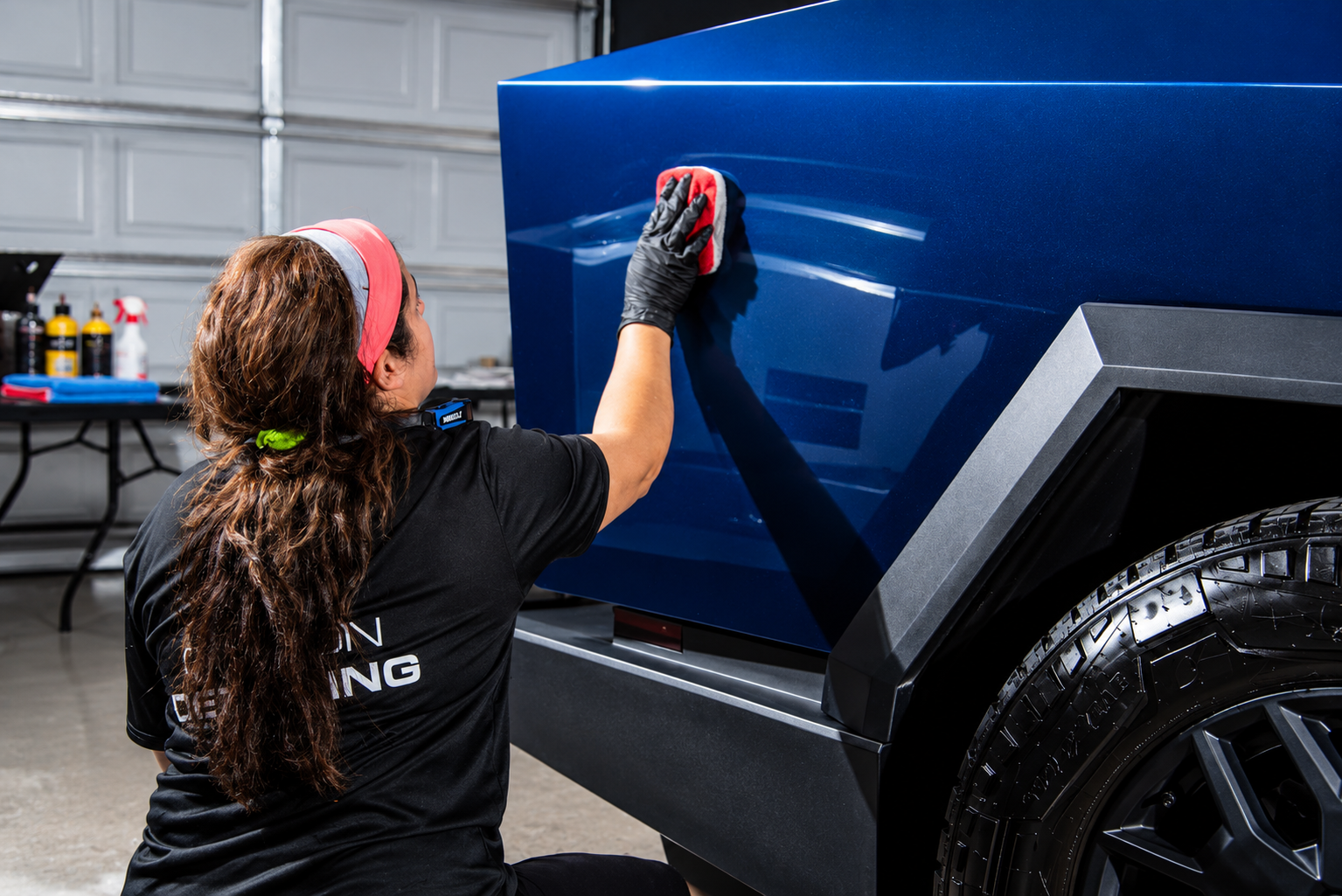 Person polishing a blue truck in a garage with a microfiber cloth