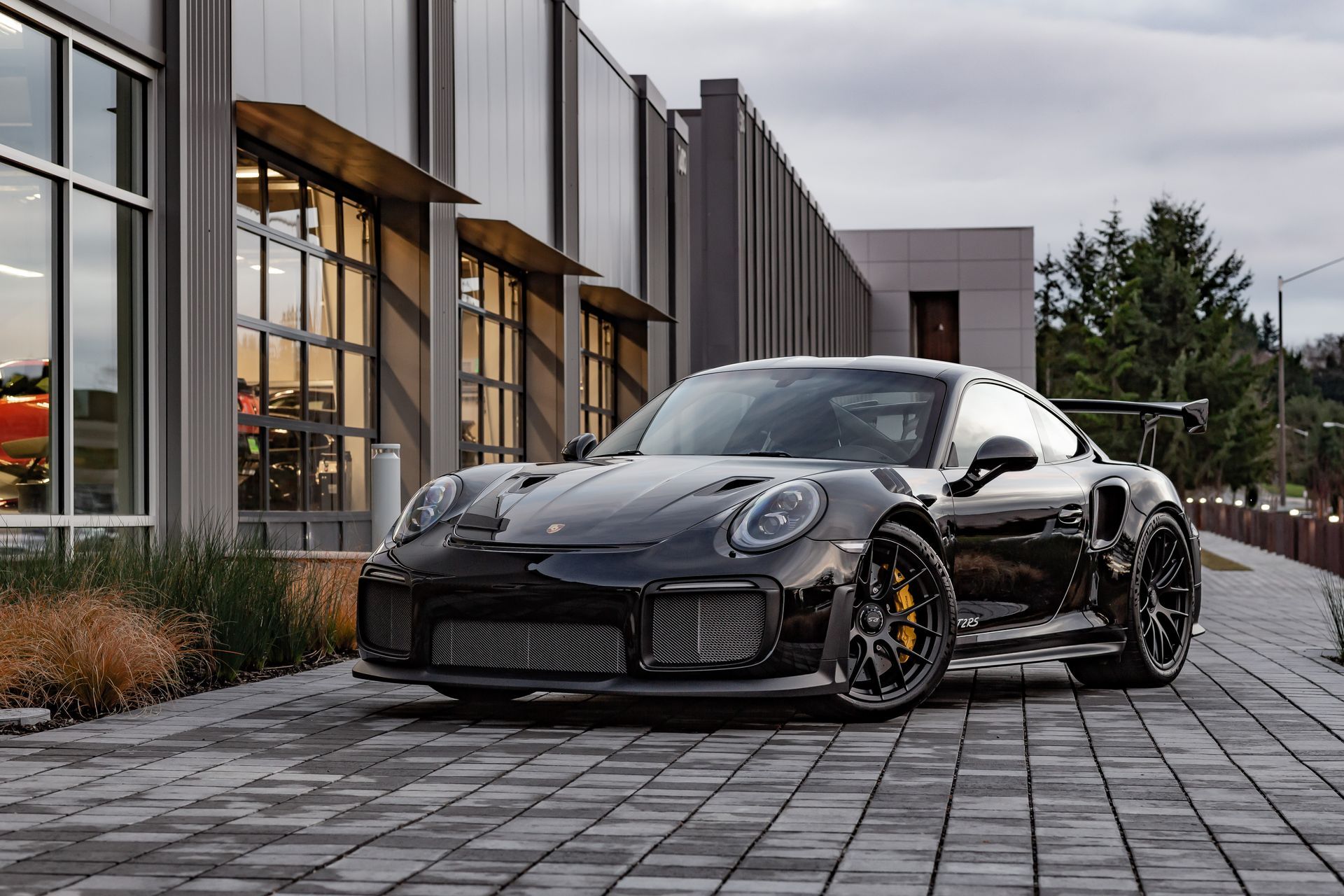 Black sports car parked on a cobblestone drive beside a modern building at dusk