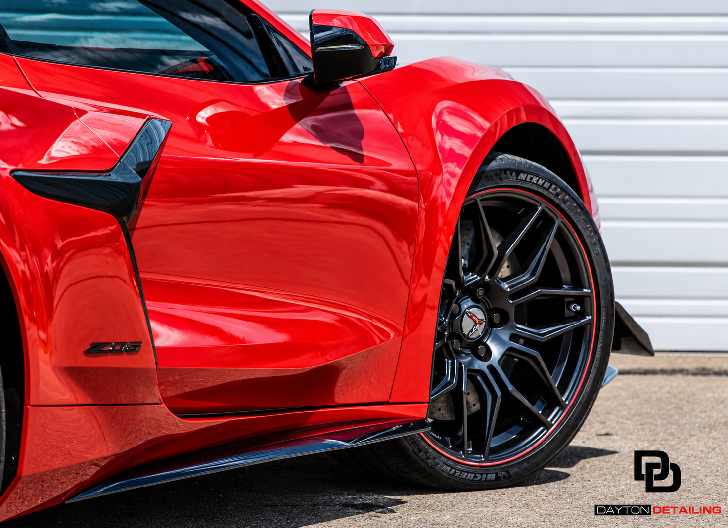 Red sports car close-up with black wheel and glossy paint against a garage door background