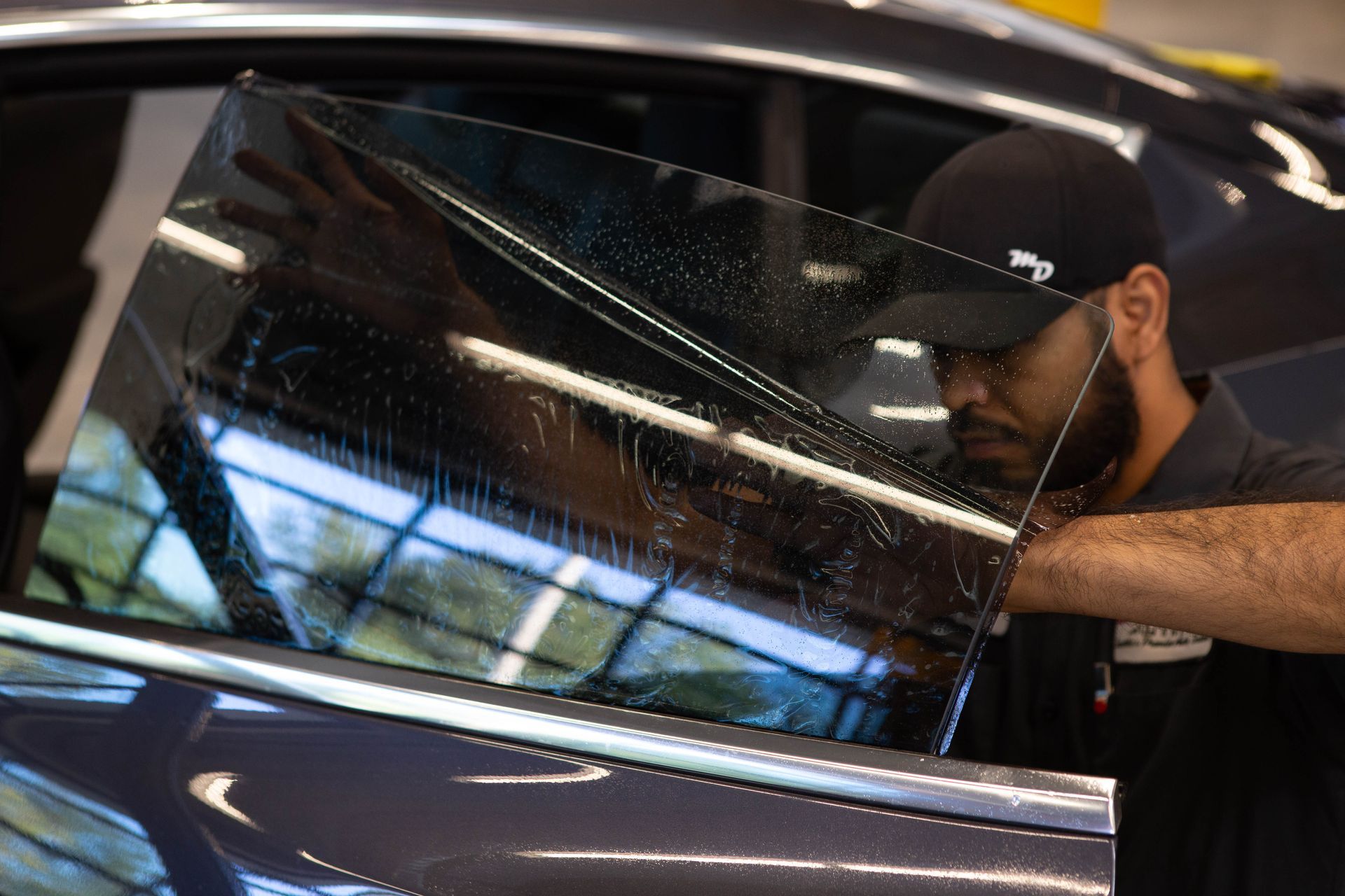 Technician applying window tint to a car side window in a garage