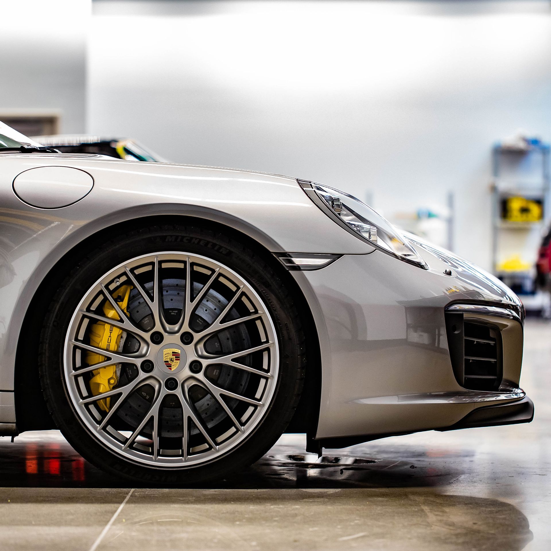Close-up of a silver sports car’s front wheel and fender in a garage