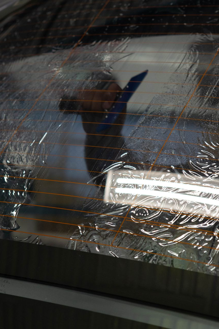 Person in a blue jacket seen through a rain-streaked car window at night