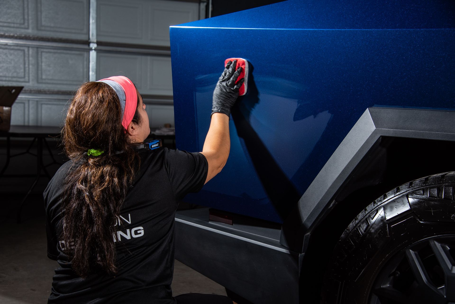 A woman is ceramic coating a blue Tesla Cybertuck with a sponge.