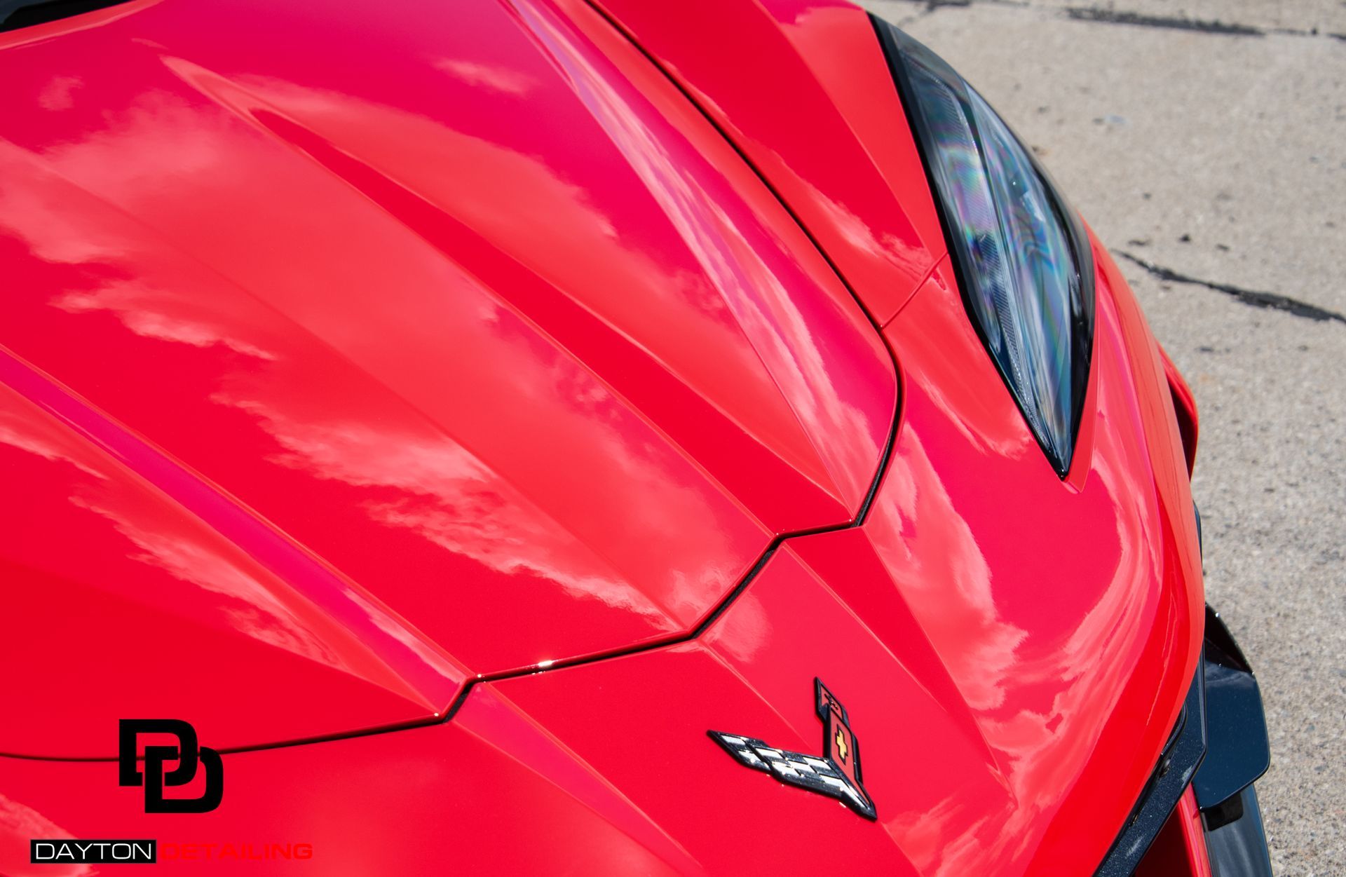 Close-up of a shiny red Corvette's hood, showcasing its emblem and sleek design.