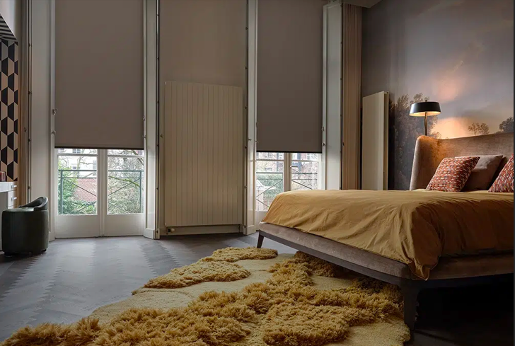 Dormitorio moderno con cama baja, alfombra de pelo largo, ventanales del suelo al techo y decoración suave en tonos neutros.