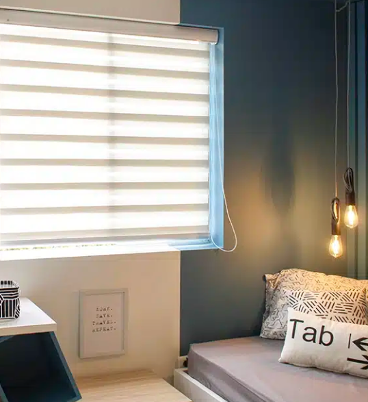 Acogedor rincón de dormitorio con persianas, cama gris, lámparas colgantes y cuadros enmarcados.