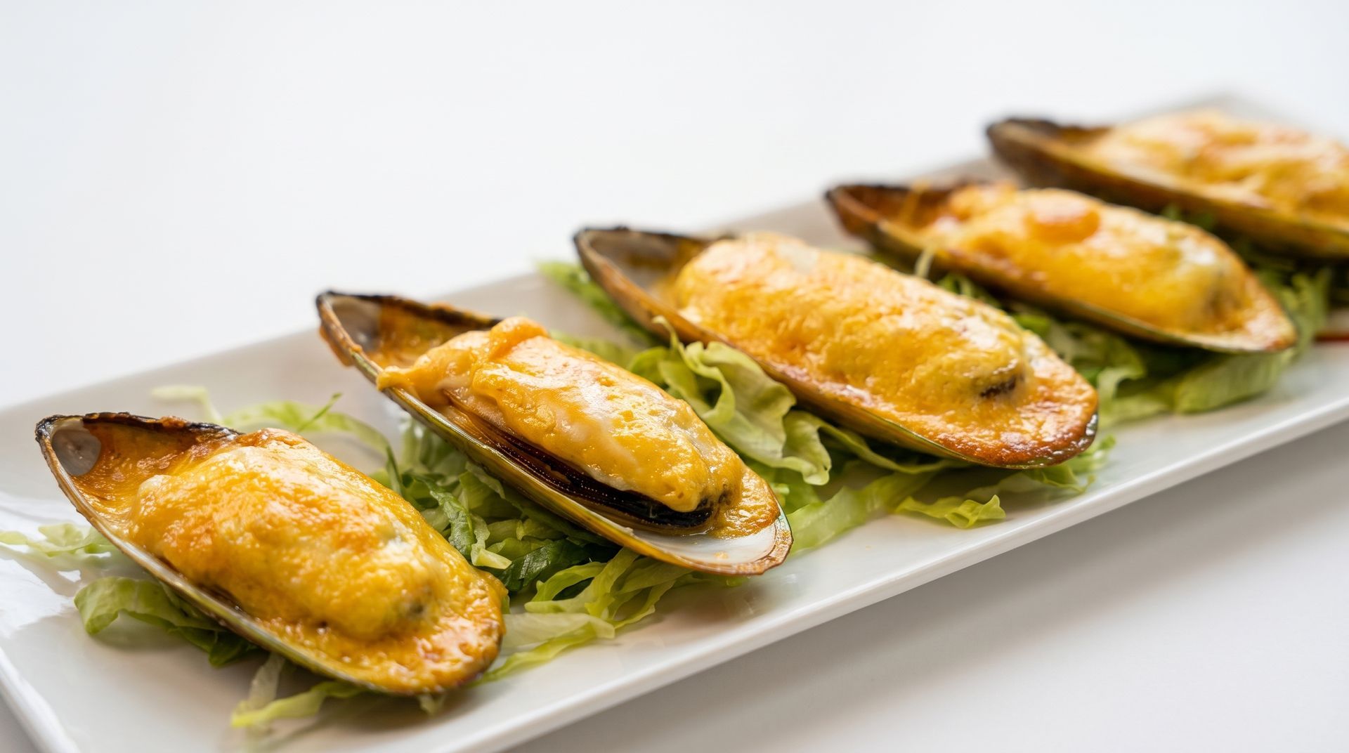 Grilled mussels topped with melted cheese on a white rectangular plate