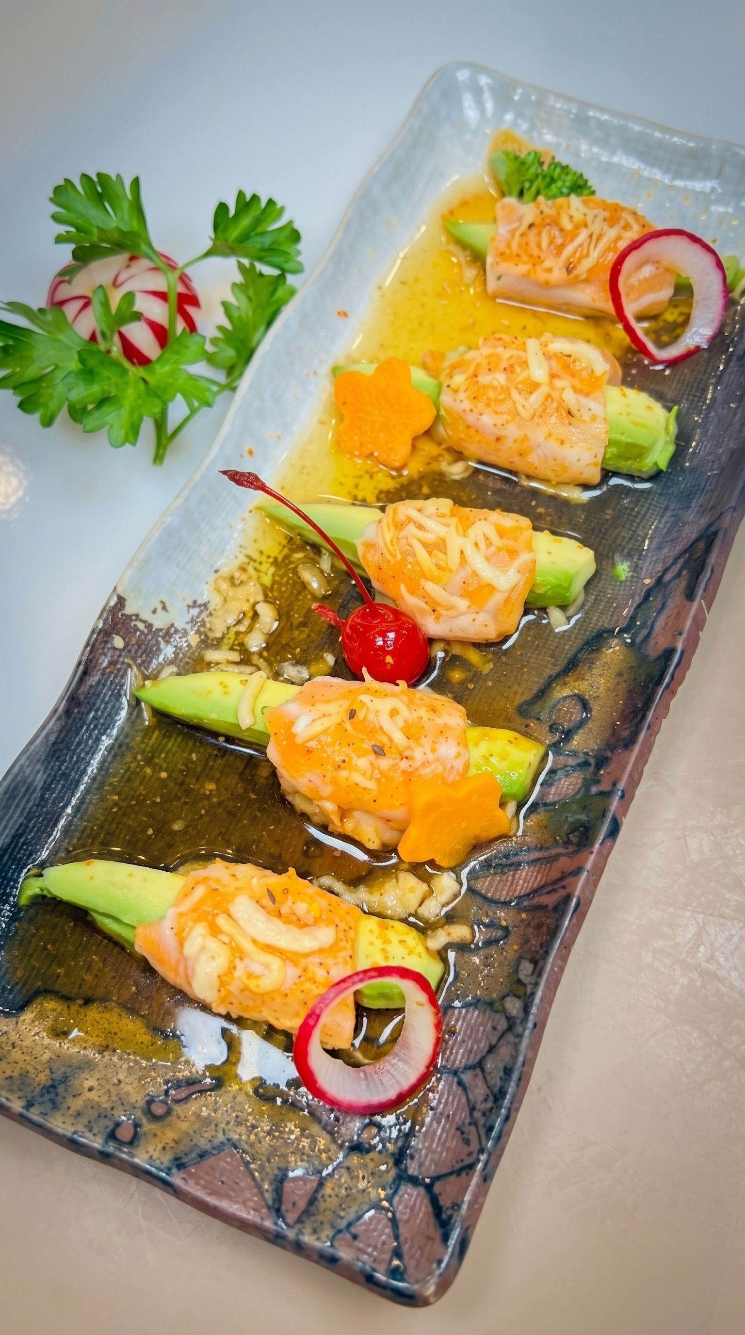 Five salmon tartare bites on avocado strips with sauce, garnished with herbs and radish on a glass plate