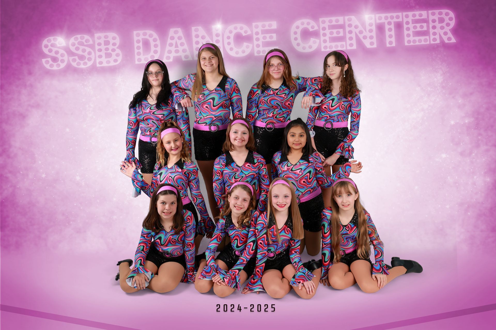 Group of children in black-and-pink dance costumes posing in a studio against a brick wall backdrop