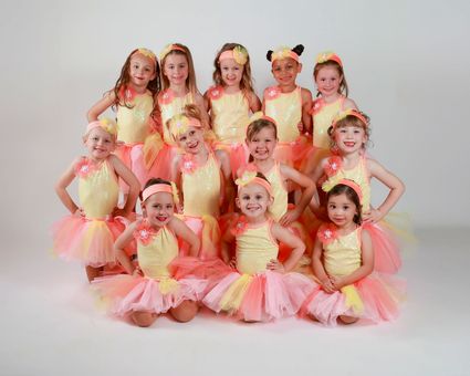 Nine children in matching pink and yellow ballet costumes posing in three rows against a white background