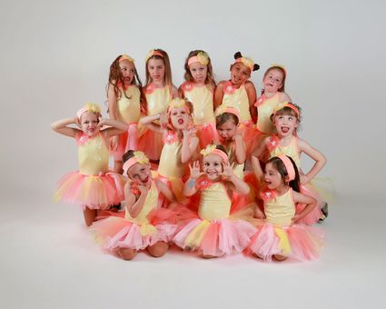 Group of children in yellow and pink ballet costumes posing in a studio