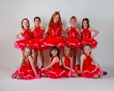 Nine children in bright red dance costumes posing in two rows against a plain white background