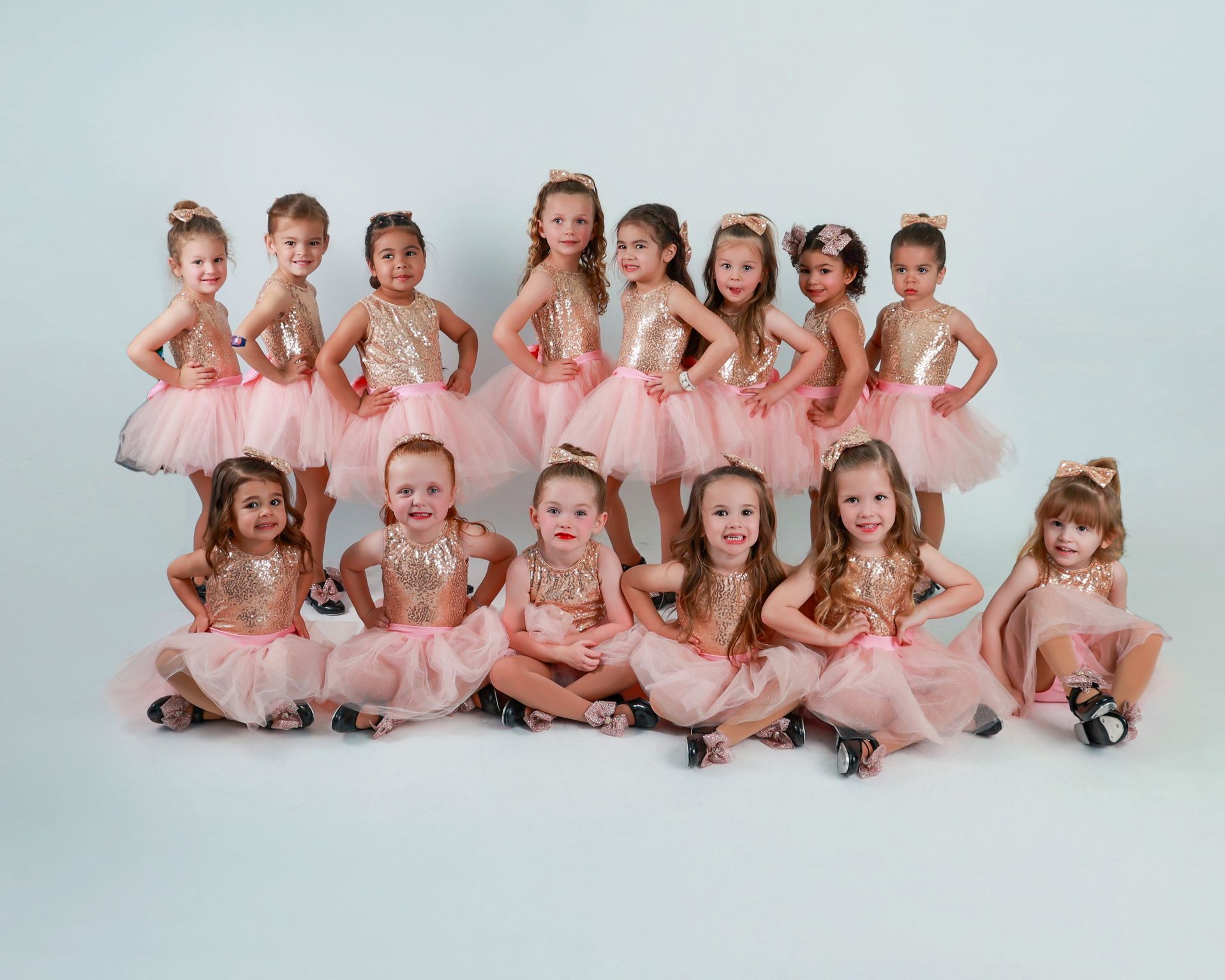 A group of children in pink ballet tutus posing in two rows on a white studio backdrop
