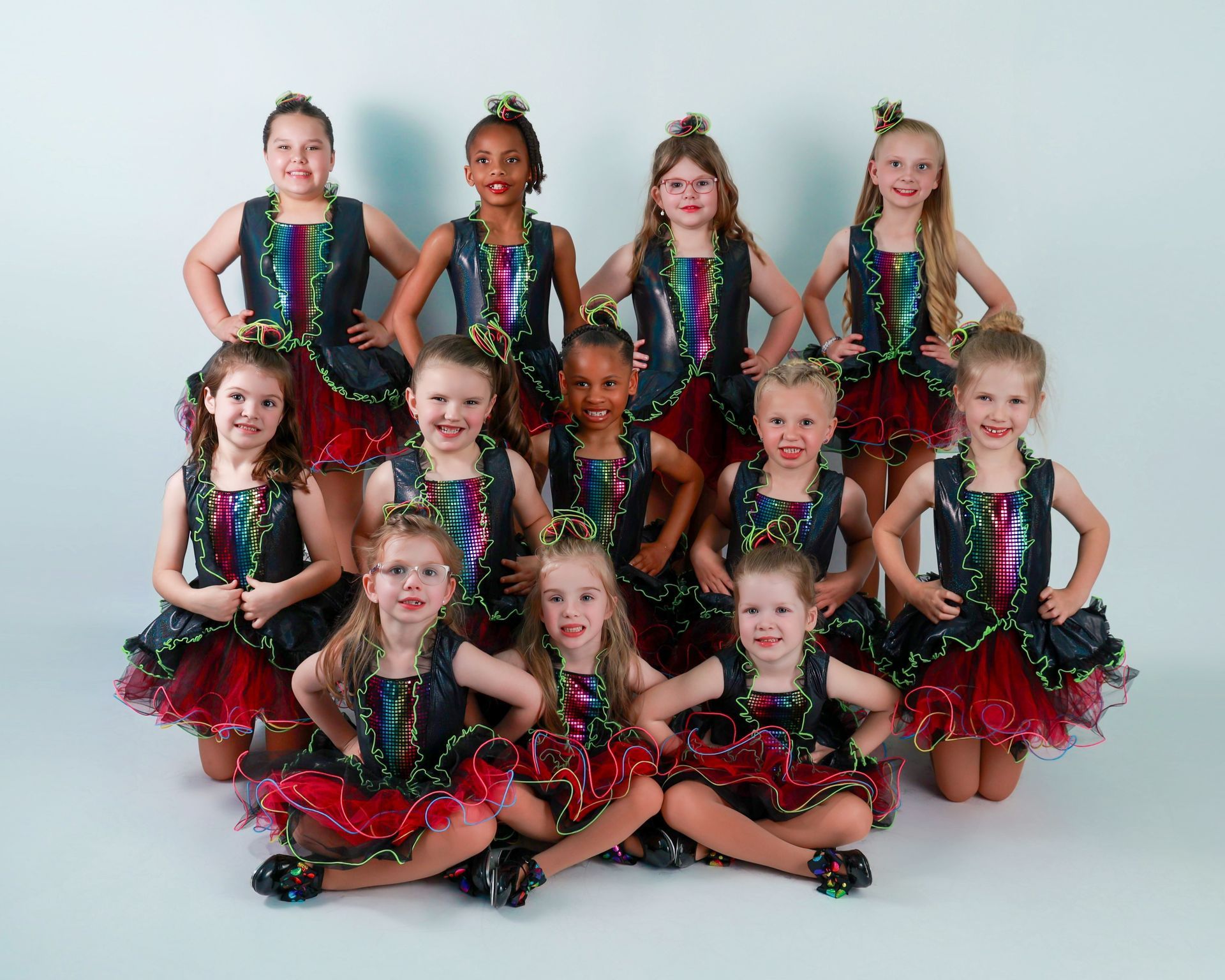Ten children in matching sequined dance costumes pose in rows against a plain studio backdrop