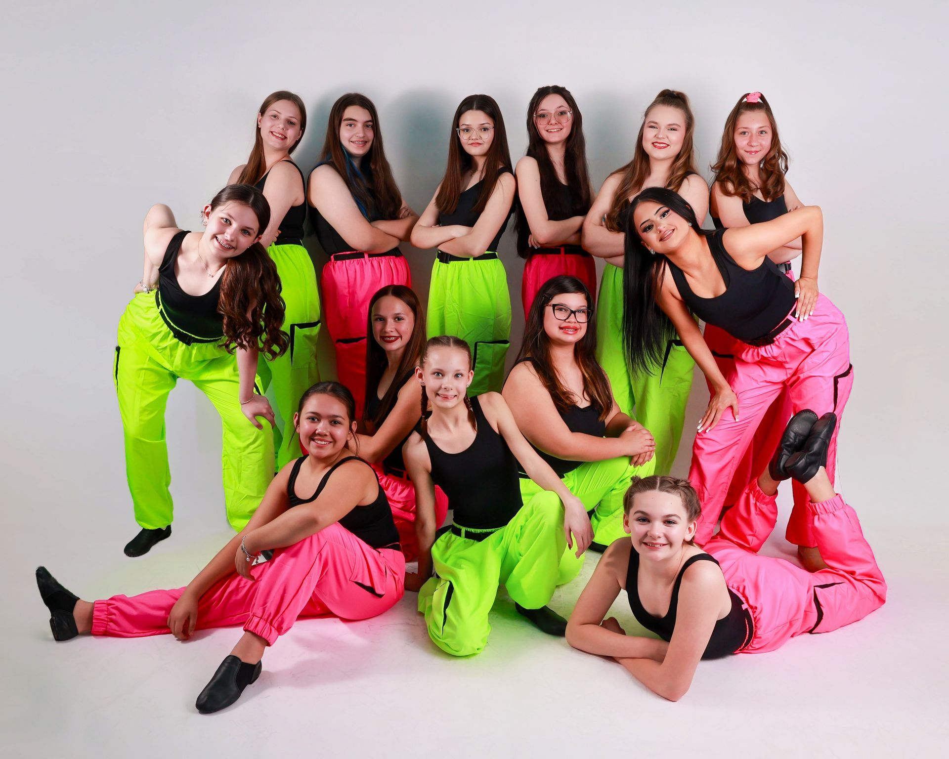 Dance center group portrait of eight dancers in neon pink and green outfits against a green backdrop