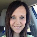 Smiling woman with long dark hair sitting in a car and looking at the camera