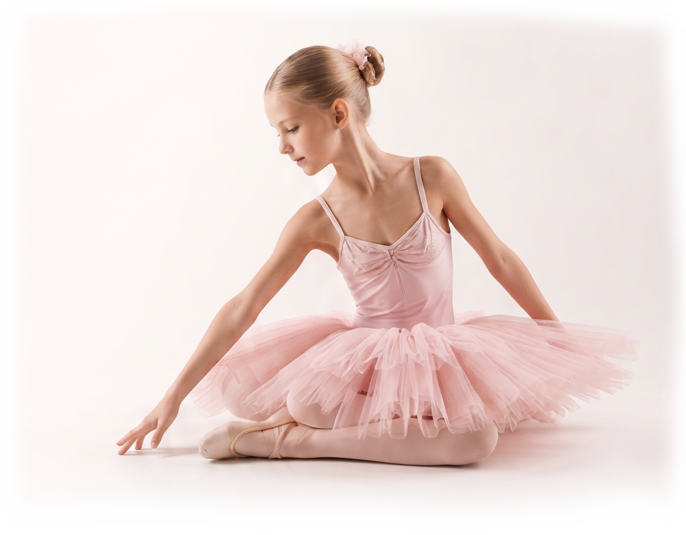 Young ballet dancer in a pink tutu seated in a graceful pose on a white background