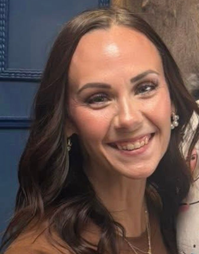 Smiling woman with long dark hair sitting in a car and looking at the camera