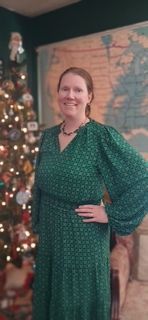 Woman in a green dress posing beside a decorated Christmas tree and wall map.