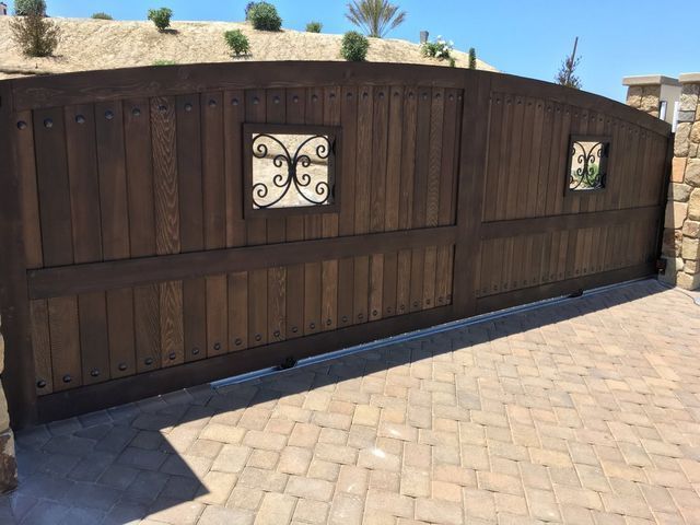 A wooden gate with a wrought iron design is sitting on a brick driveway.