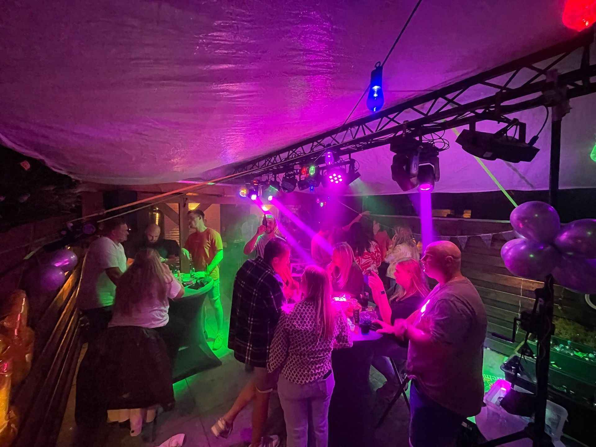 Mensen dansen op een buitenfeest met paarse en groene lichten.