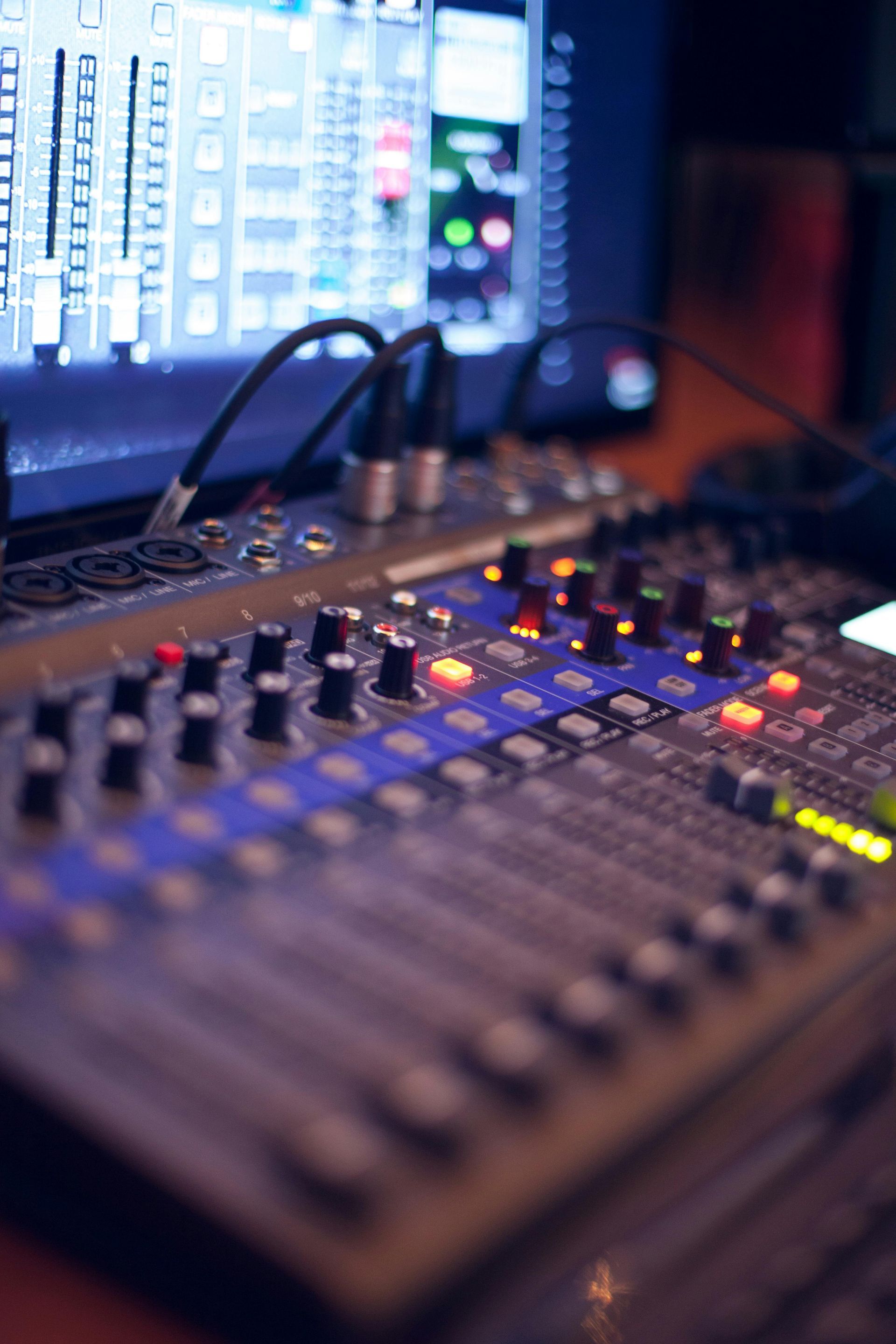 Audiomengpaneel met knoppen, faders en een computermonitor op de achtergrond.