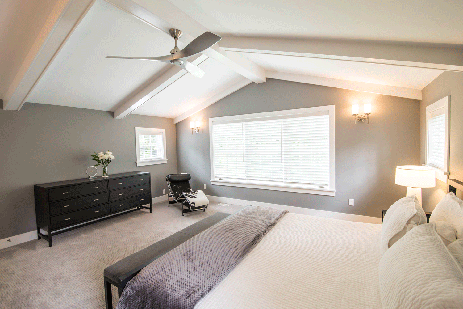 A bedroom with a bed , dresser , chair and ceiling fan.