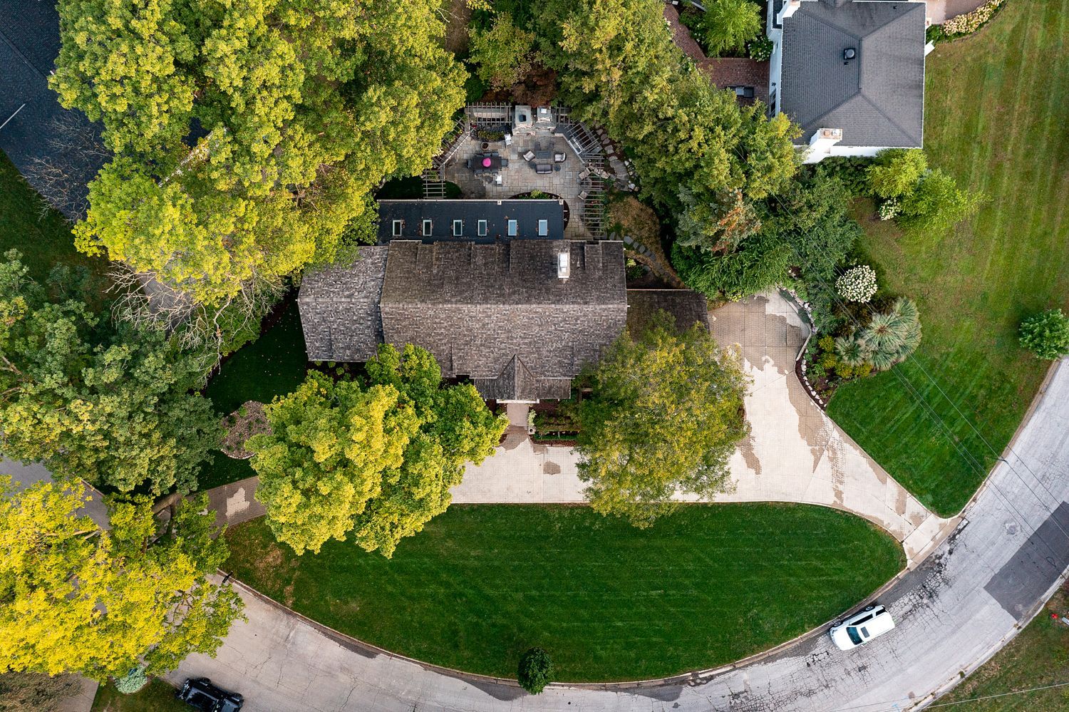 Aerial view of a house with a dark roof, surrounded by trees, lawn, and a curving driveway.