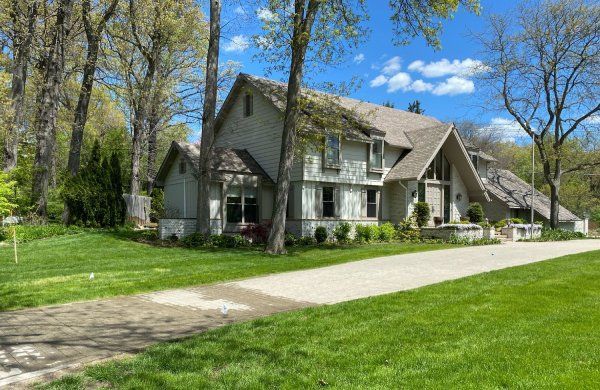 A large house is sitting on top of a lush green hillside surrounded by trees.