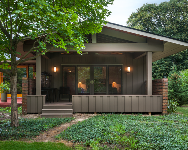 A small house with a porch and a tree in front of it