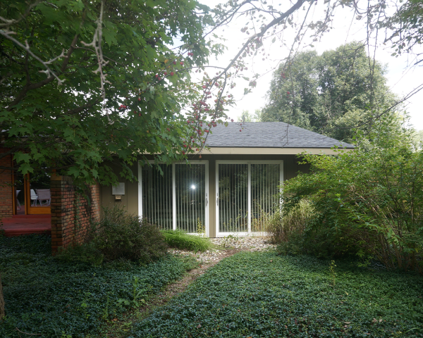 A house with sliding glass doors is surrounded by trees and bushes