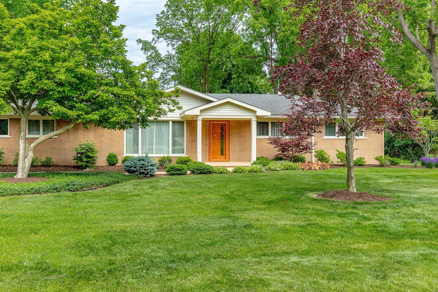 A brick house with a lush green lawn and trees in front of it.