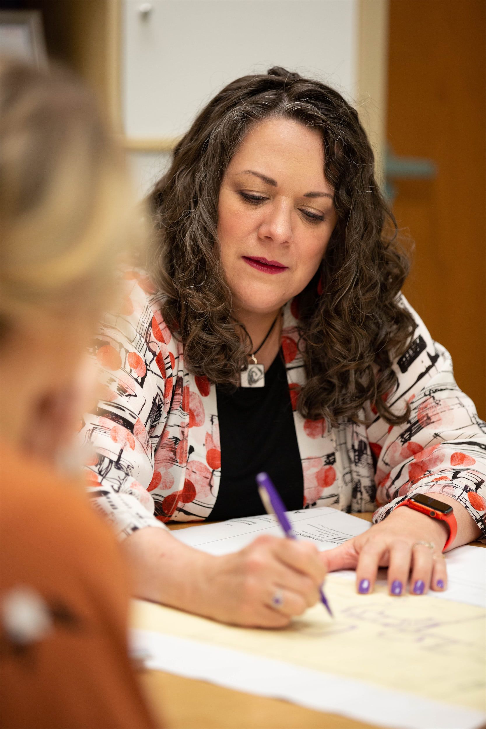 A woman in a floral shirt is sitting at a table