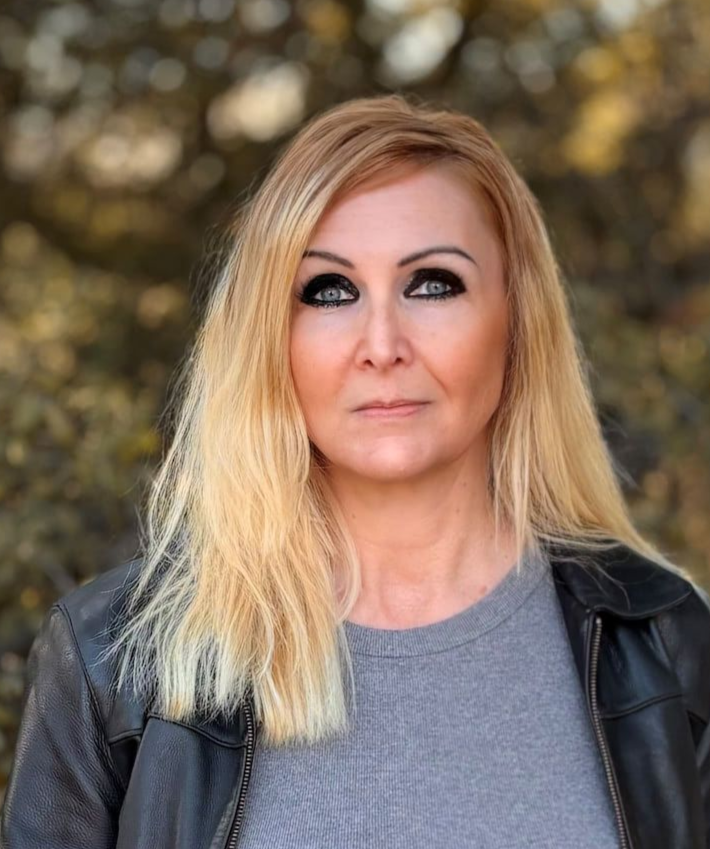 A woman with blonde hair is wearing a black dress and looking at the camera.