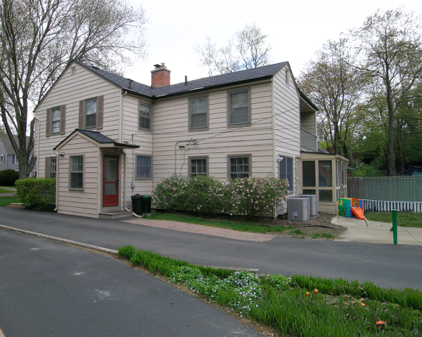 A large white house with a red door is sitting on the side of a road.