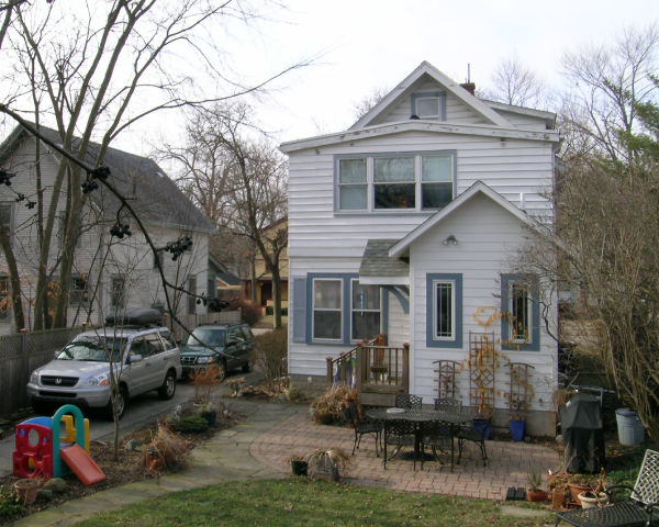 A white house with blue shutters sits in a residential neighborhood