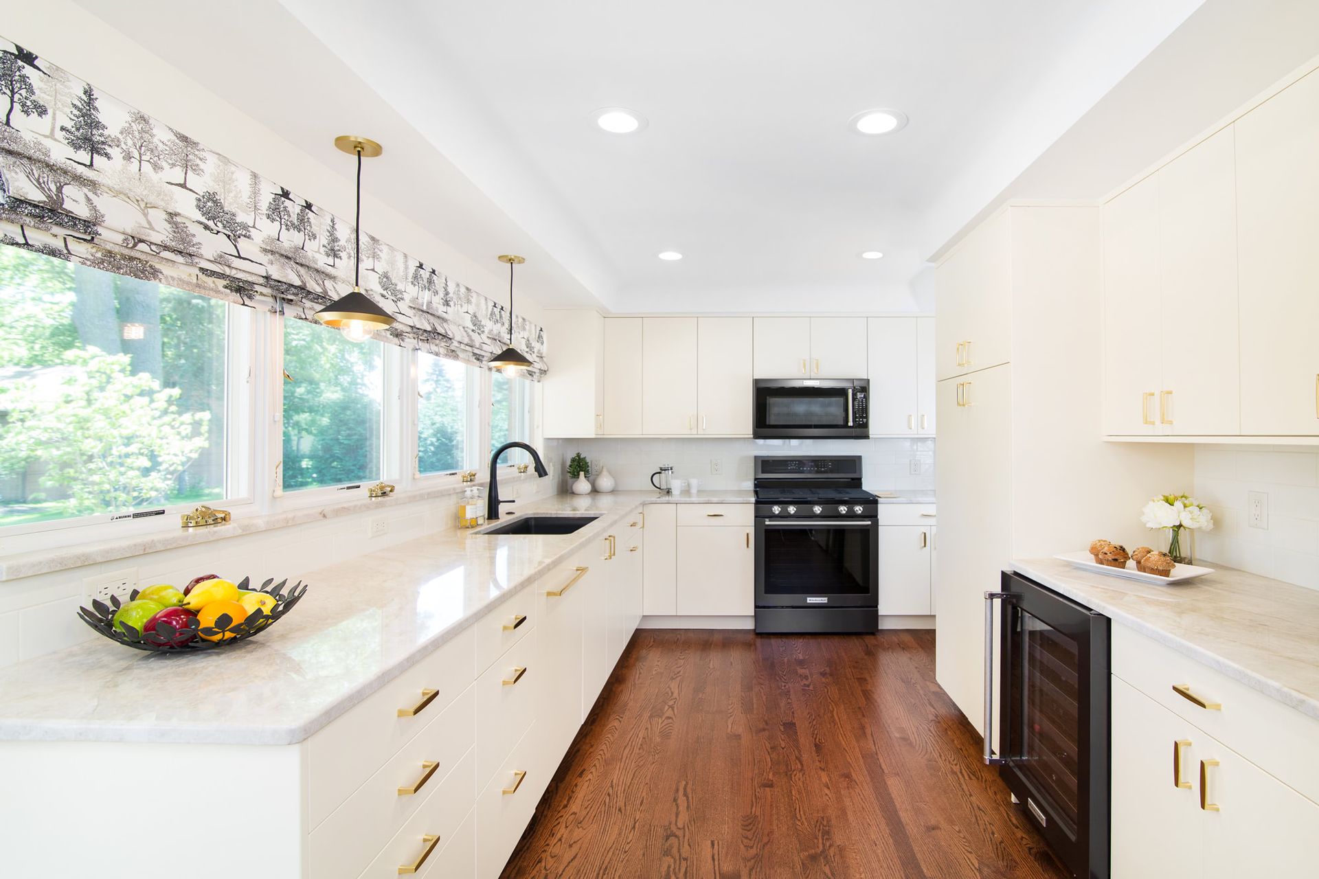 A kitchen with white cabinets , stainless steel appliances , hardwood floors and a bowl of fruit on the counter.