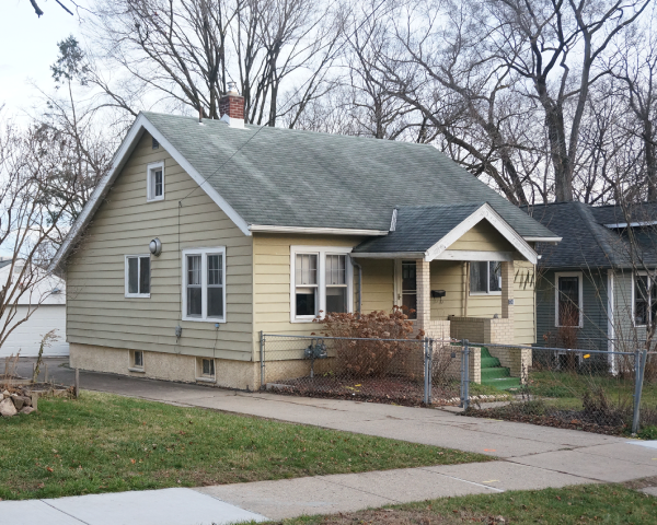 A yellow house with a green roof and a porch