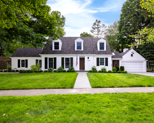 A white house with black shutters and a lush green lawn.