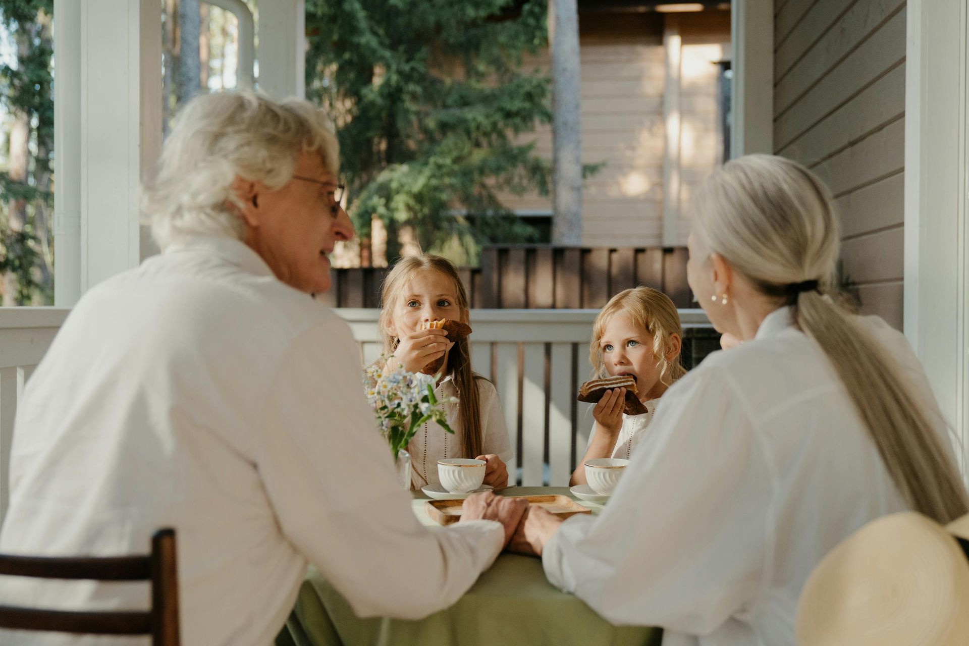 A family is sitting at a table on a porch eating food.