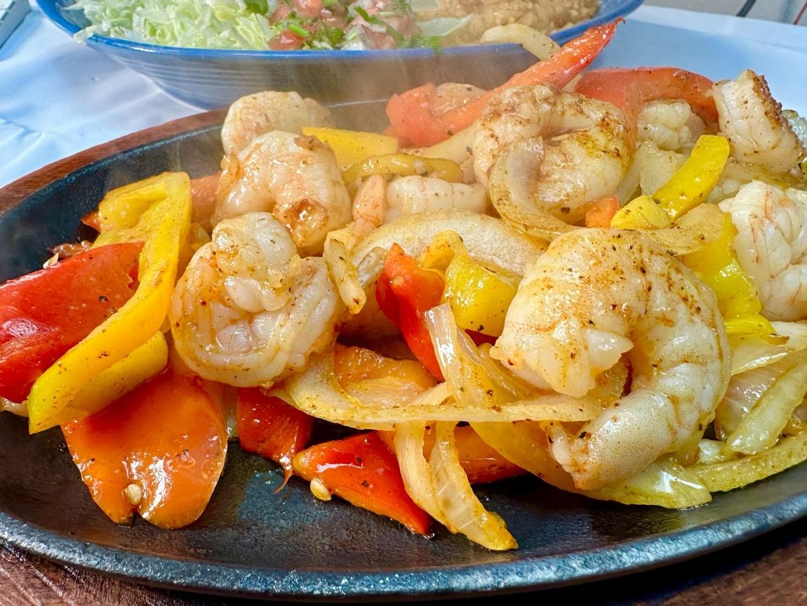 Sizzling shrimp fajitas with yellow and red bell peppers, onions, served on a hot plate.