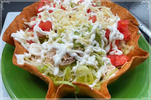 Taco salad in a fried tortilla bowl with lettuce, tomato, cheese, and dressing.