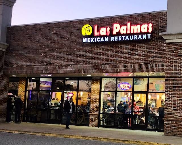Las Palmas Mexican Restaurant exterior, brick building, glass windows, patrons dining, neon sign.